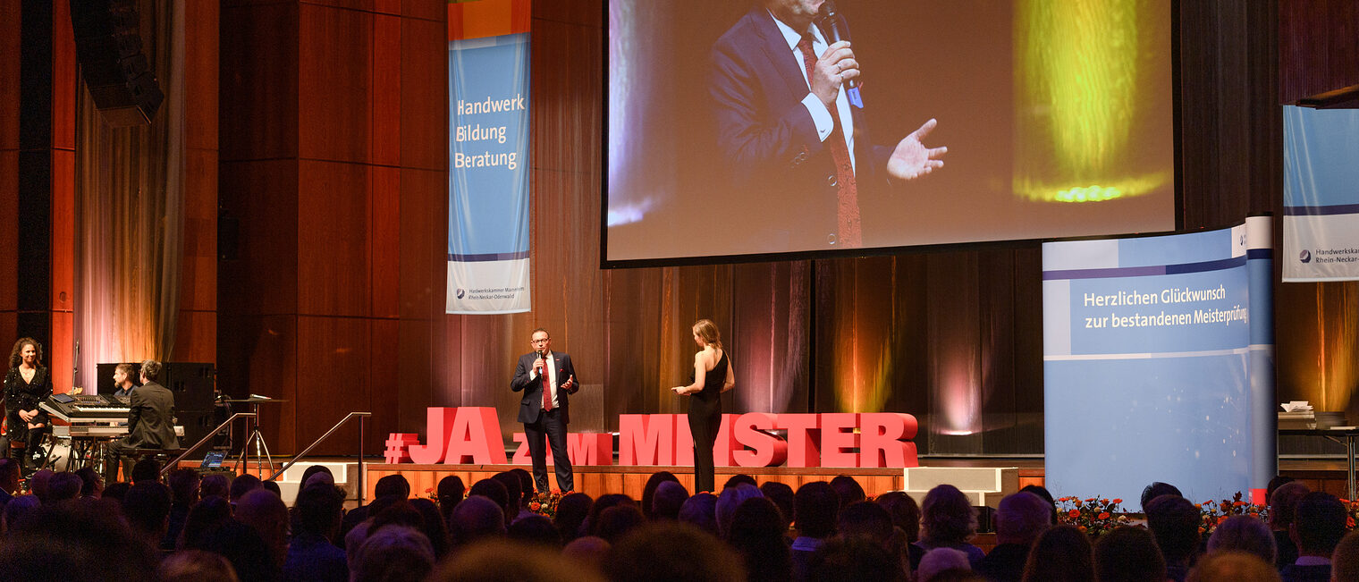 Handwerkskammerpräsident Klaus Hofmann wird von der Moderatorin Janina Klabes interviewt. Das Foto zeigt den Blick auf die Bühne aus der 10. Reihe.