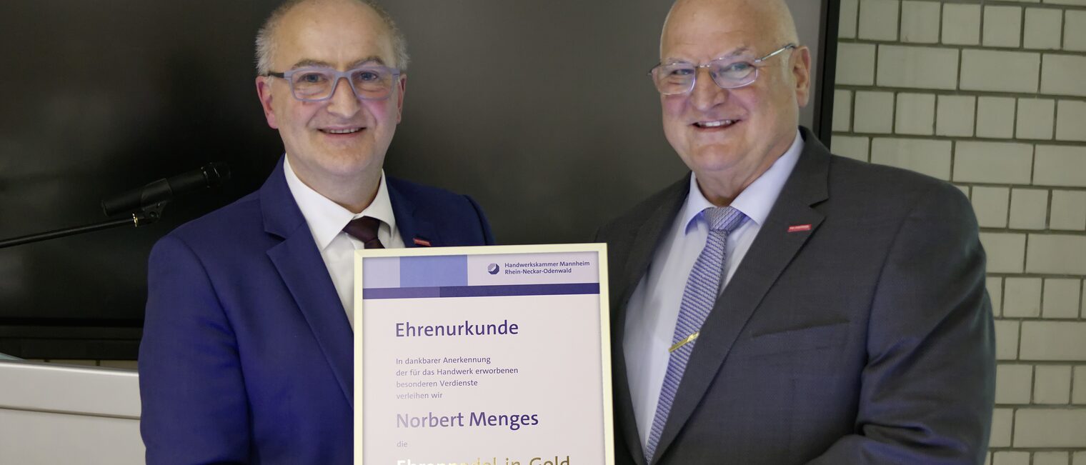 Langjähriges Vorstandsmitglied erhält Ehrennadel in Gold mit Urkunde Rechts Norbert Menges. Links Steffen Haug. Beide Herren in dunklem Anzug und weißem Hemd. In der Mite die Ehrenurkunde.