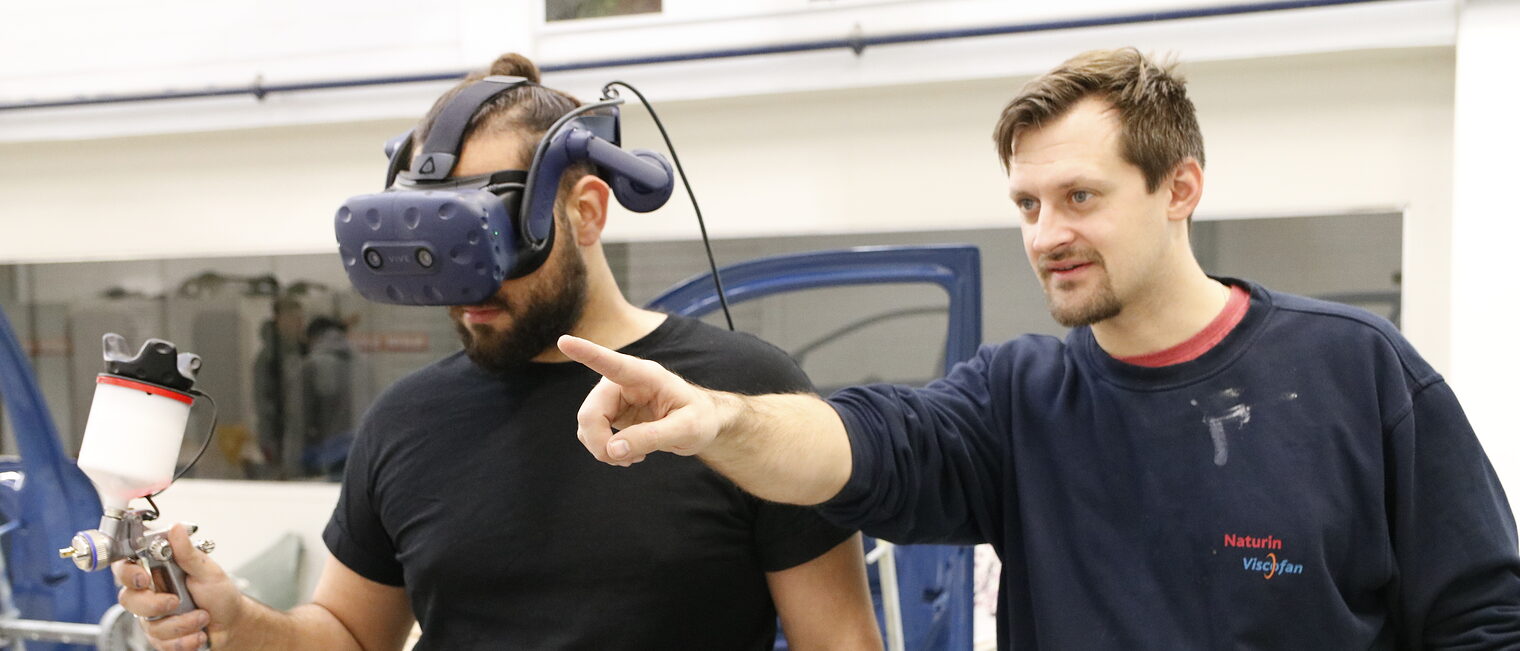 Ausbilder mit Lehrling. Lehrling hat die VR-Brille auf. 