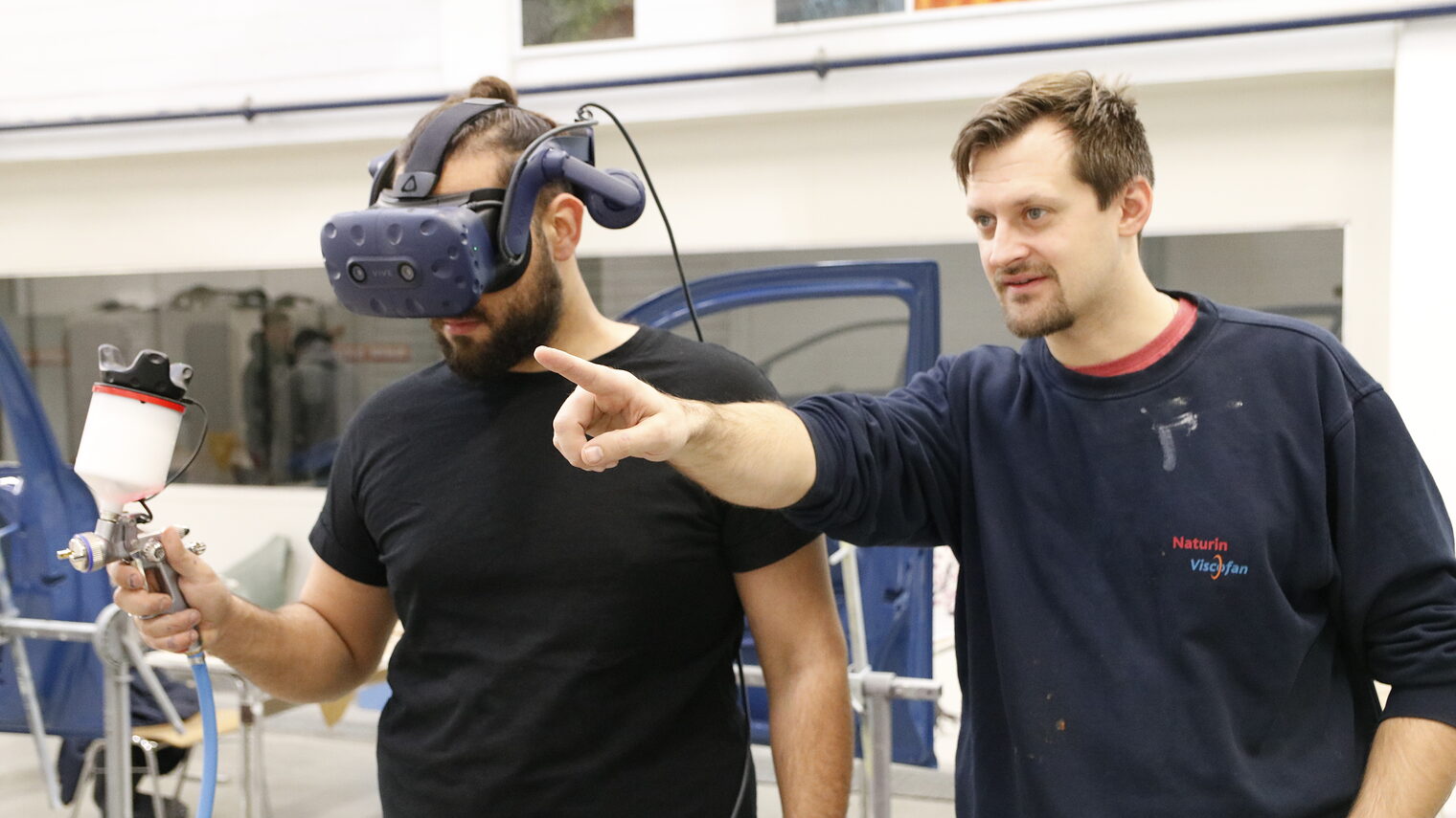 Ausbilder mit Lehrling. Lehrling hat die VR-Brille auf. 