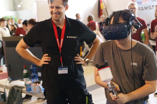 Ausbilder Timo Potsch zeigt interessiertem Schüler den Umgang mit der Farbspritzpistole als virtuelles Erlebnis mit der VR-Brille