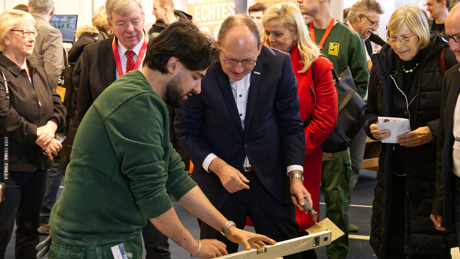 Bürgermeister Specht setzt einen Stein auf eine bereits vorbereitete Mauer auf der Messe Jobs for Future. 