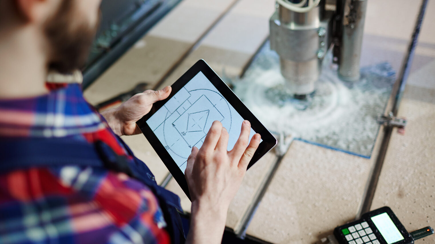 Handwerker an einer Fräsmaschiene mit einem Tablet in der Hand