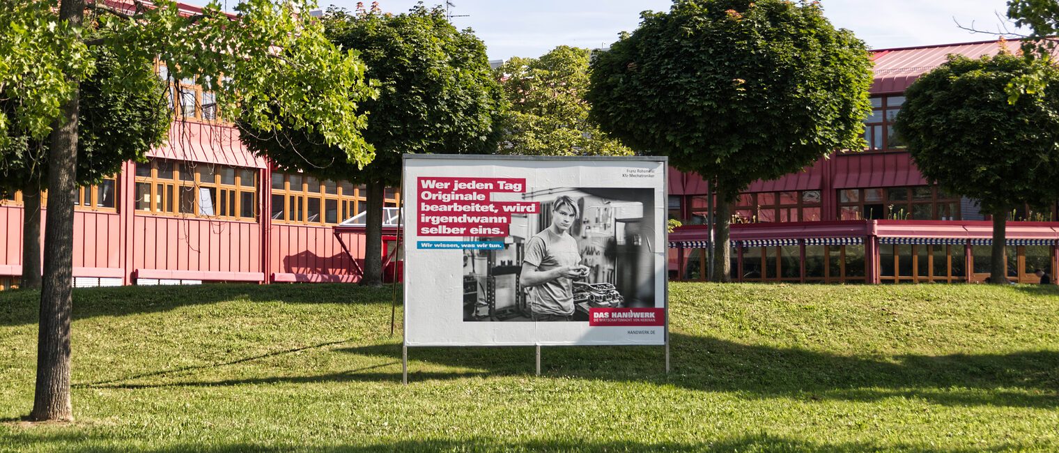 Plakatwand vor der Bildungsakademie, mit der Aufschrift: Wer jeden Tag Originale bearbeitet, wird irgendwann selber eins.