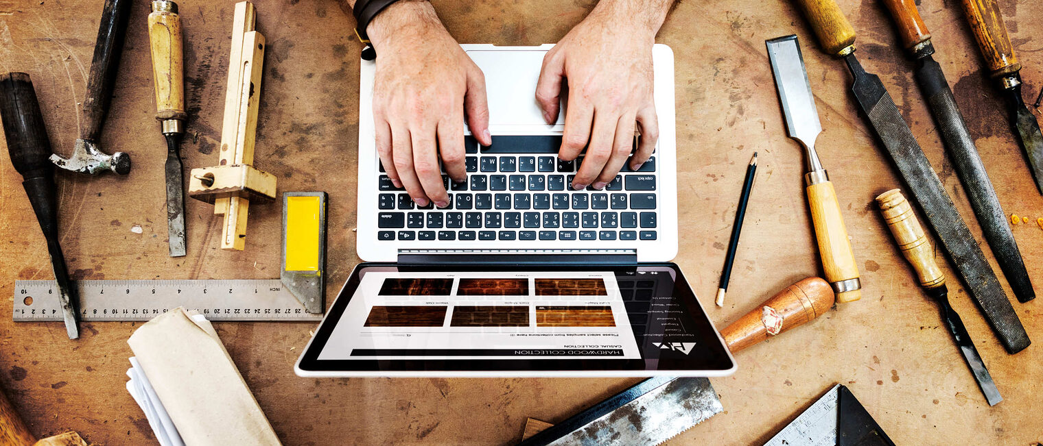 Mann tippt auf einem Laptop, der mitten auf einem Werktisch steht, umgeben von allerlei Werkzeugen