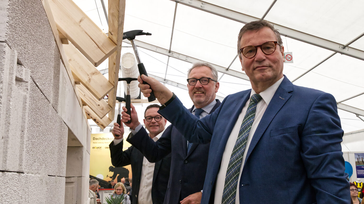 Drei Männer mit einem Hammer in der Hand schlagen Nägel in eine Holzleiste