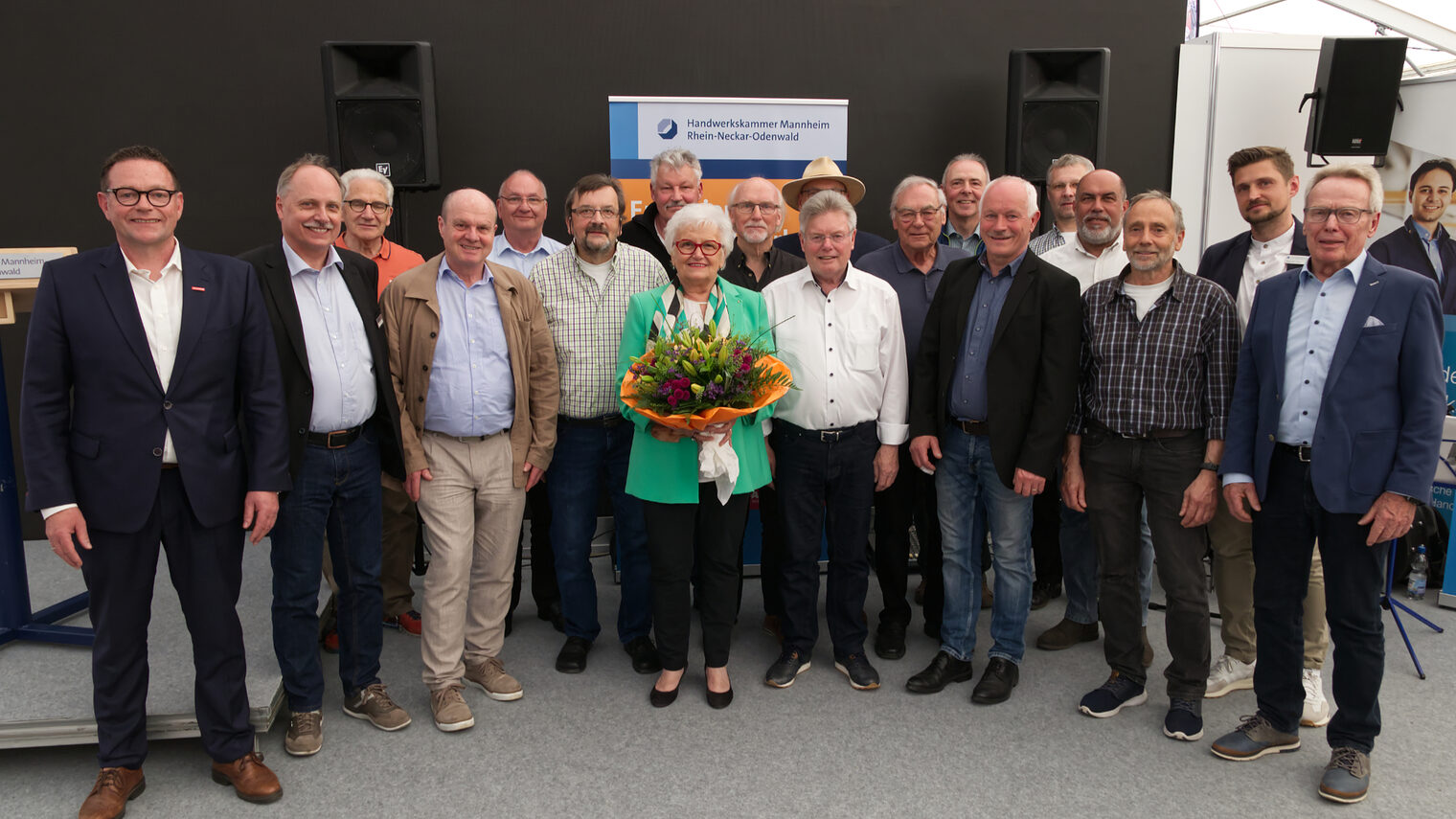 16 Prüfer in einem Halbkreis aufgestellt. die Prüferin in der Mitte mit einem Blumenstrauß. Präsident Hofmann ganz links. 