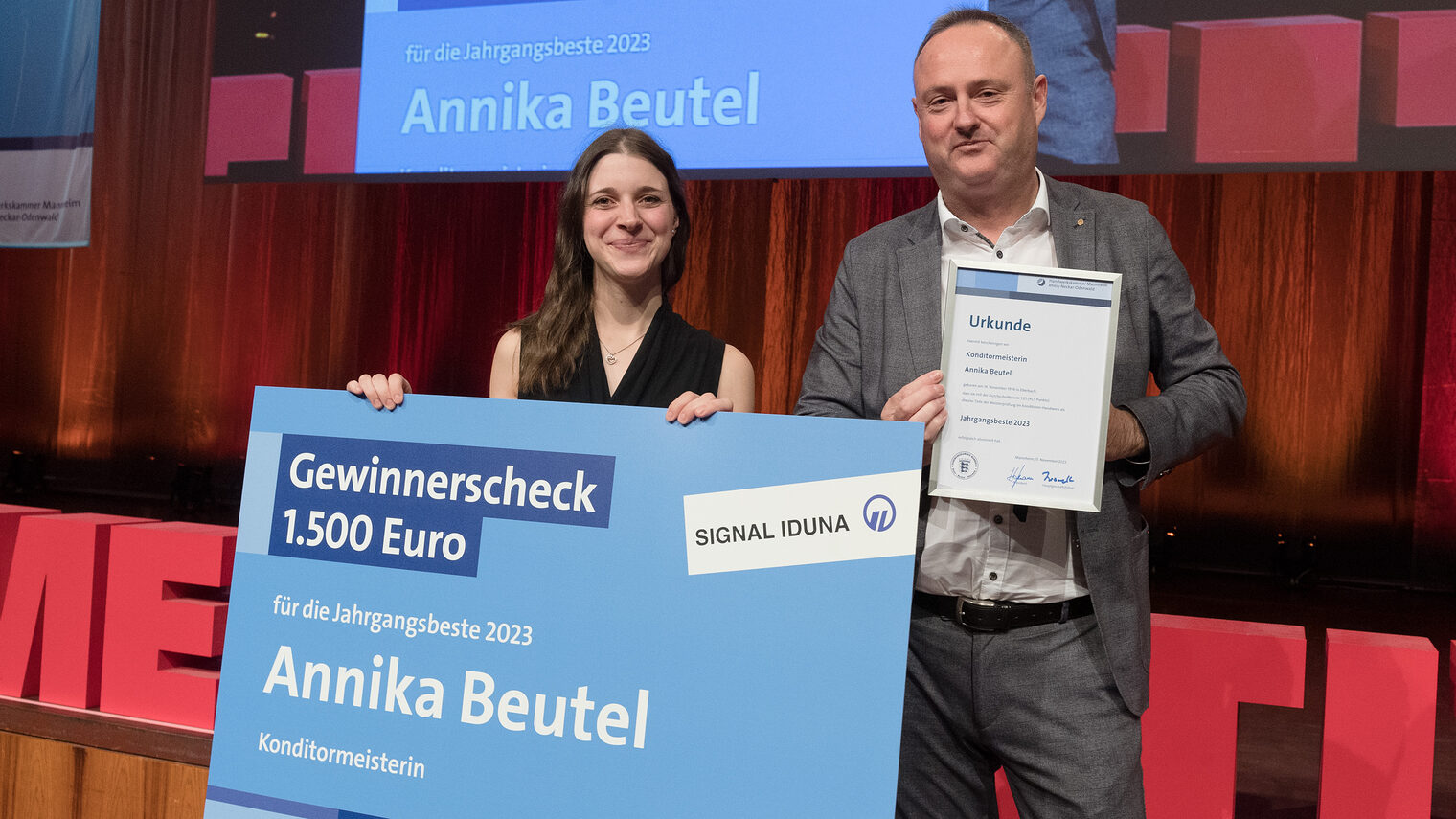 Frau Beutel hält zusammen mit Herrn Bauer den Scheck in die Kamera. 