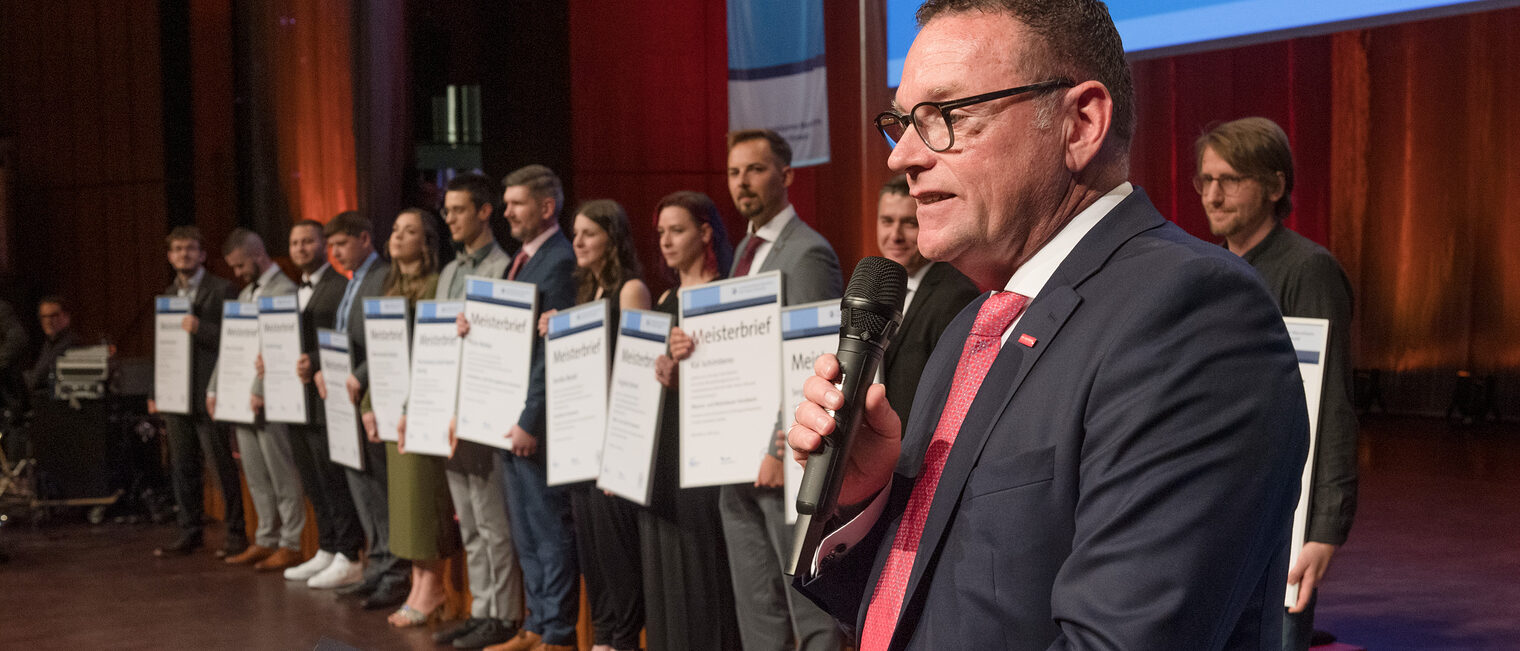 Handwerkskammerpräsident Klaus Hofmann bei der Erhenbunsrede mit den Jahrgangsbesten Meisterinnen und Meistern im Hintergrund.