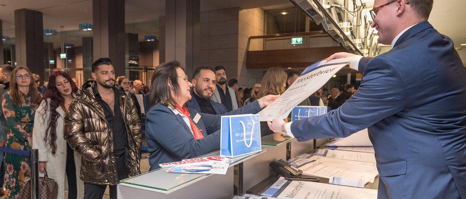 Zu sehen ist die Ausgabe der Meisterbriefe an einem Counter im Congresscenter Rosengarten. Die Meisterbriefe werden dort berreicht. 