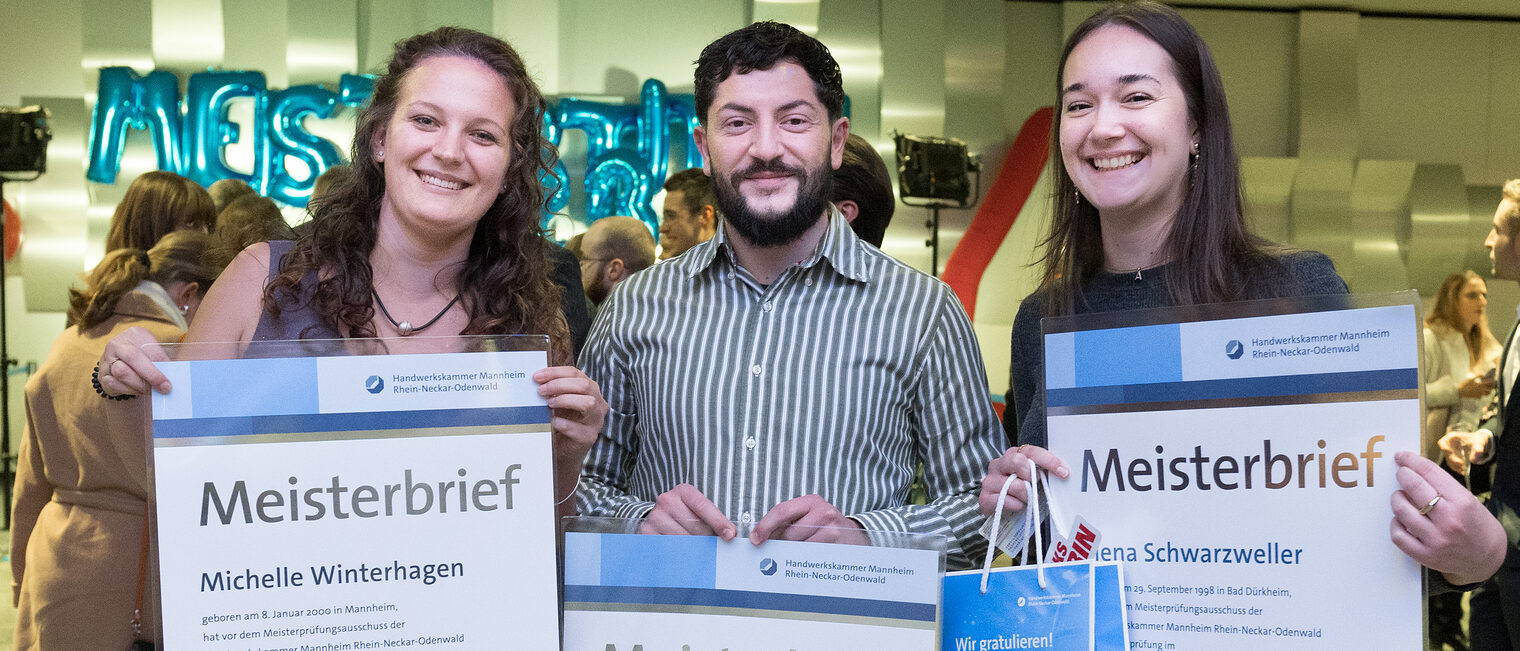 Zwei stolze Meisterinnen und ein Meister präsentieren Ihren Meisterbrief im Foyer des Congresscenters Rosengarten in Mannheim.