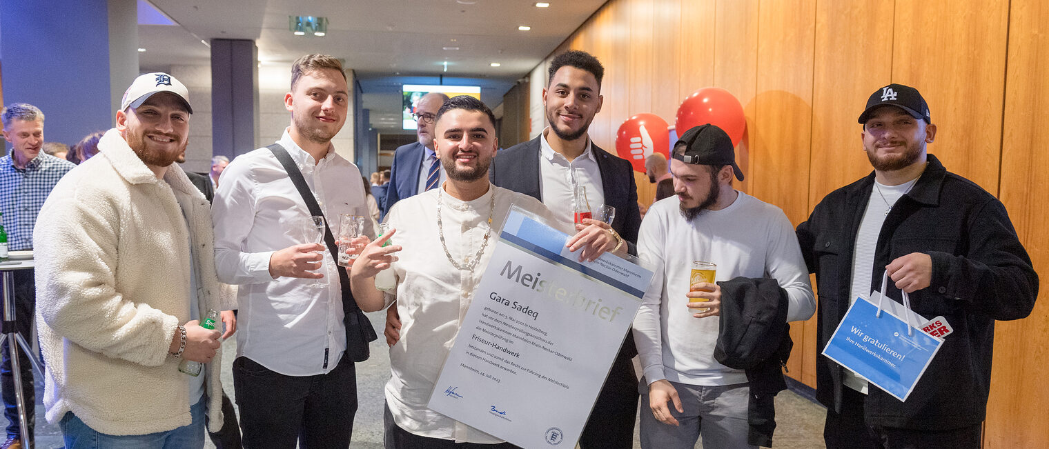 Friseurmeister Gara Sadeq h&auml;lt stolz seinen Meisterbrief in der Hand und ist umringt von f&uuml;nf Freunden. 