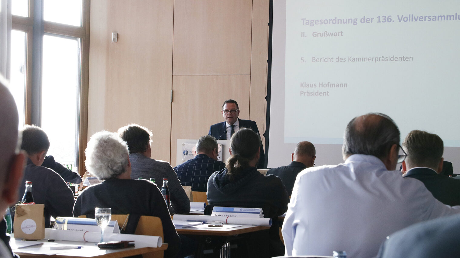 Sitzungsmitglieder bei der Tagung der 136. Vollversammlung im Sitzungssaal der Bildungsakademie mit Blick auf Präsident Hofmann am Rednerpult