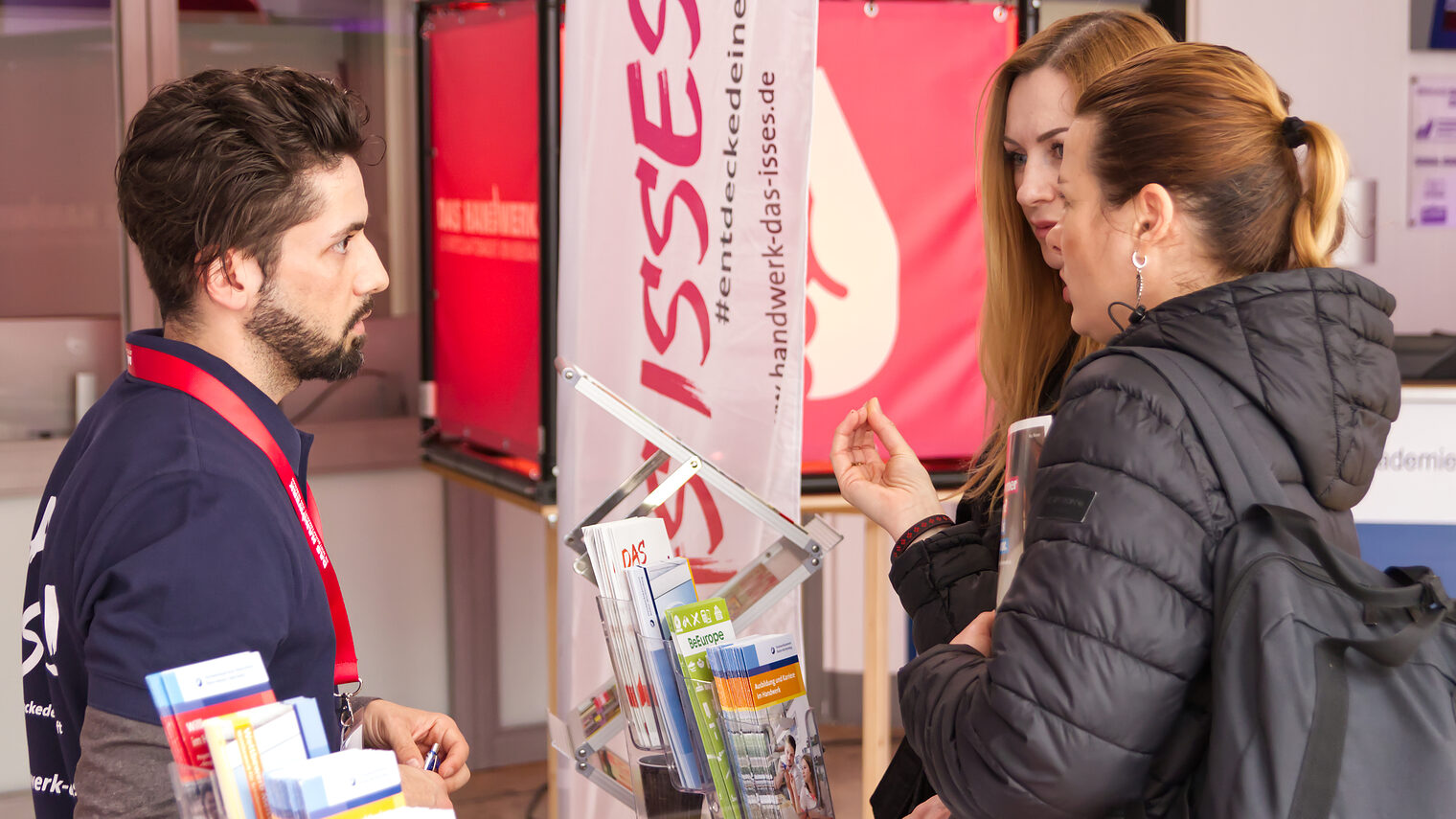 Zwei junge Frauen informieren sich beim Ausbildungsberater am Stand der Handwerkskammer.