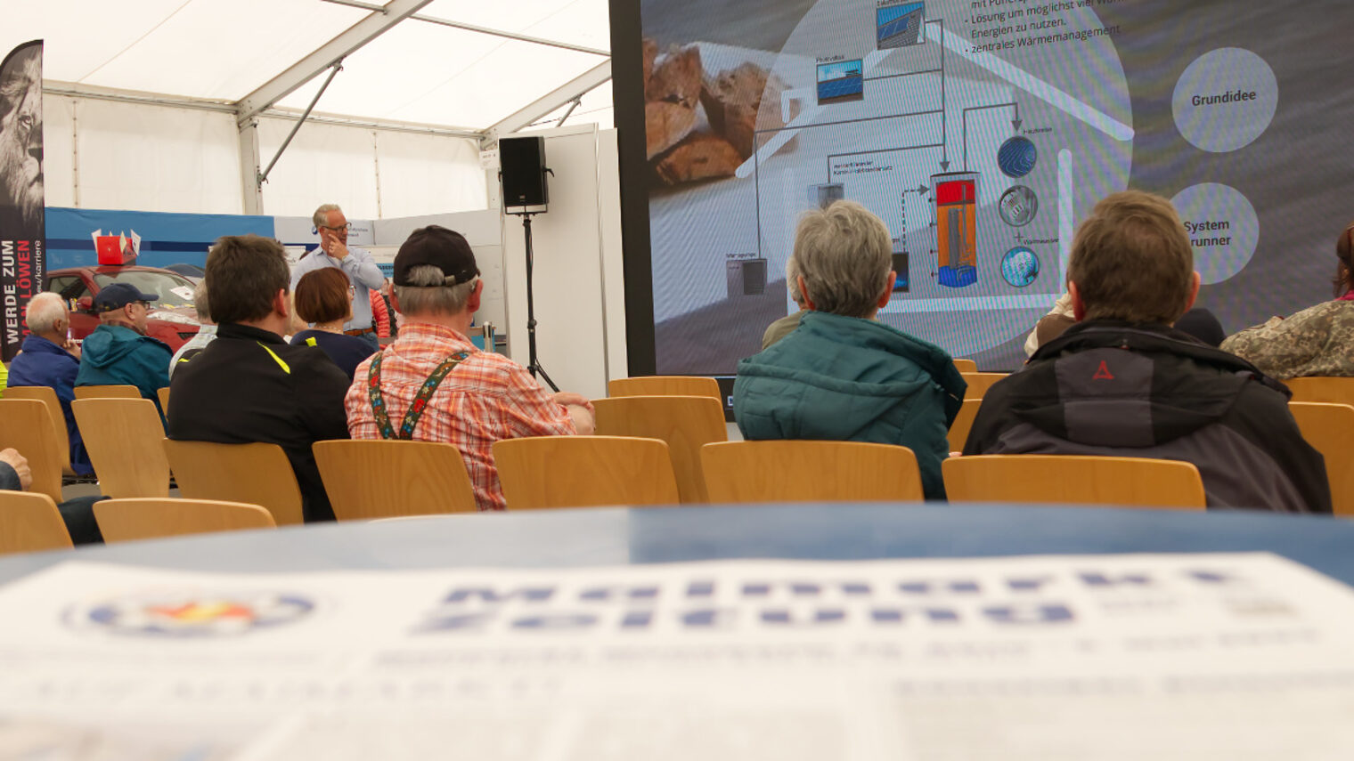 Präsentation vor einer Videoleinwand mit Zuhörern