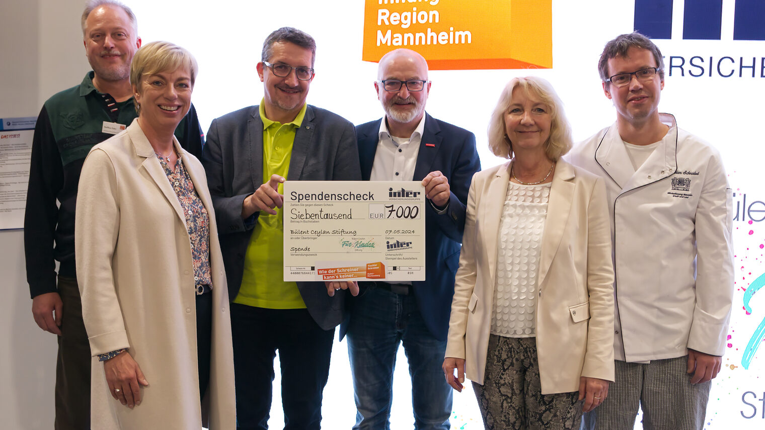 Sechs Personen stellen sich dem Fotografen mit einem Scheck