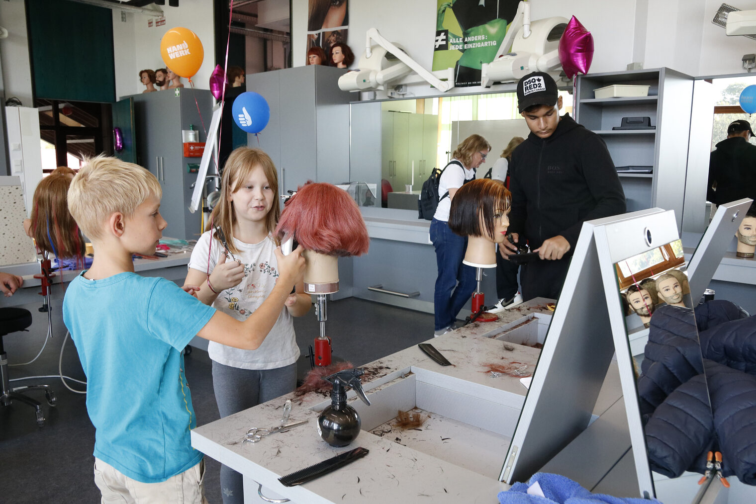 Kinder probieren sich an einem Frisierkopf mit Kamm und Schere aus. 
