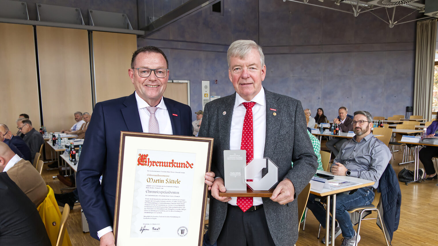 Präsident Hofmann, links, hält die Ehrenurkunde von Herrn Sättele in den Händen, da Herr Sättele, rechts, selbst die Stele in den Händen hält. 
