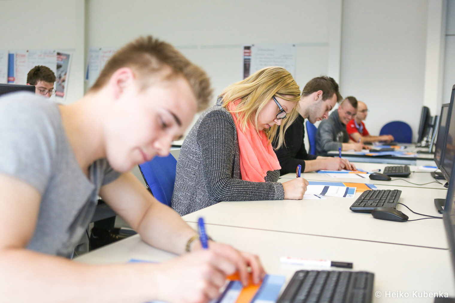 Teilnehmende eines Seminars schreiben auf Arbeitsblätter Auszubildende nhmen an einem Seminar teil und schreiben auf Arbeitsblätter, während sie vor Computern sitzen
