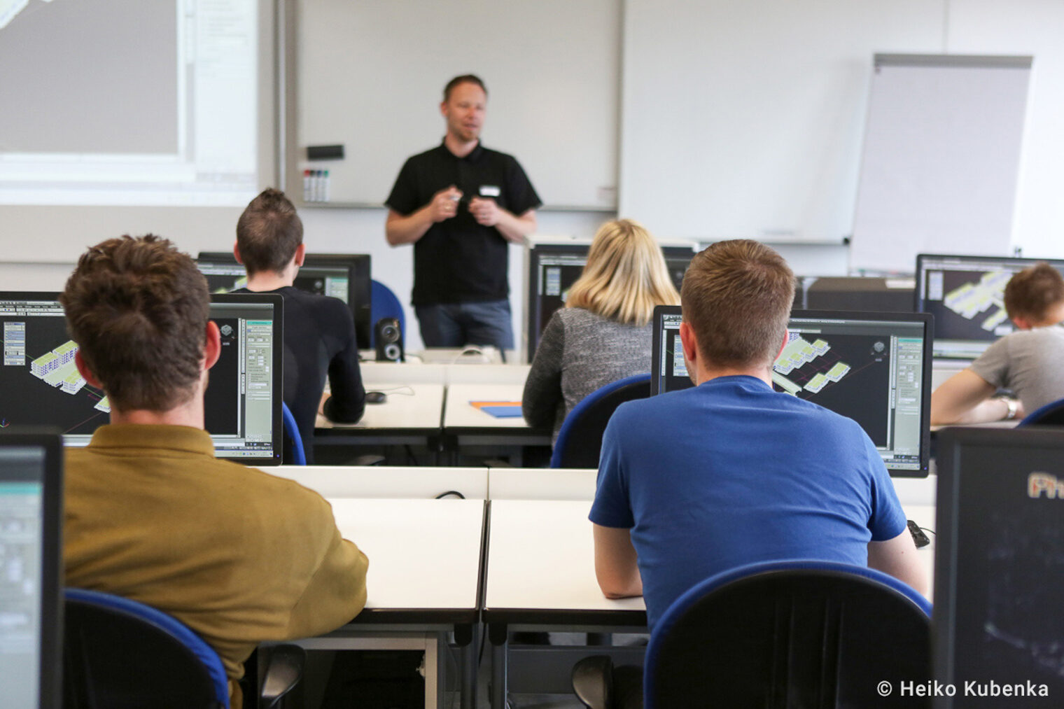 Schüler verfolgen den Unterricht Ihres Lehrers in einem Computerraum Auszubildende sitzen im Unterricht vor Ihren Computern und hören aufmerksam dem Lehrer zu