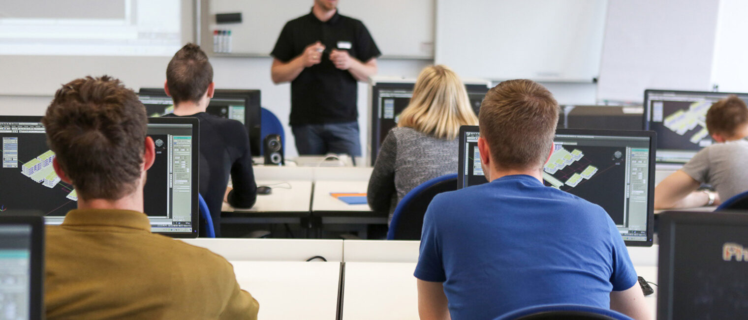Schüler verfolgen den Unterricht Ihres Lehrers in einem Computerraum Auszubildende sitzen im Unterricht vor Ihren Computern und hören aufmerksam dem Lehrer zu