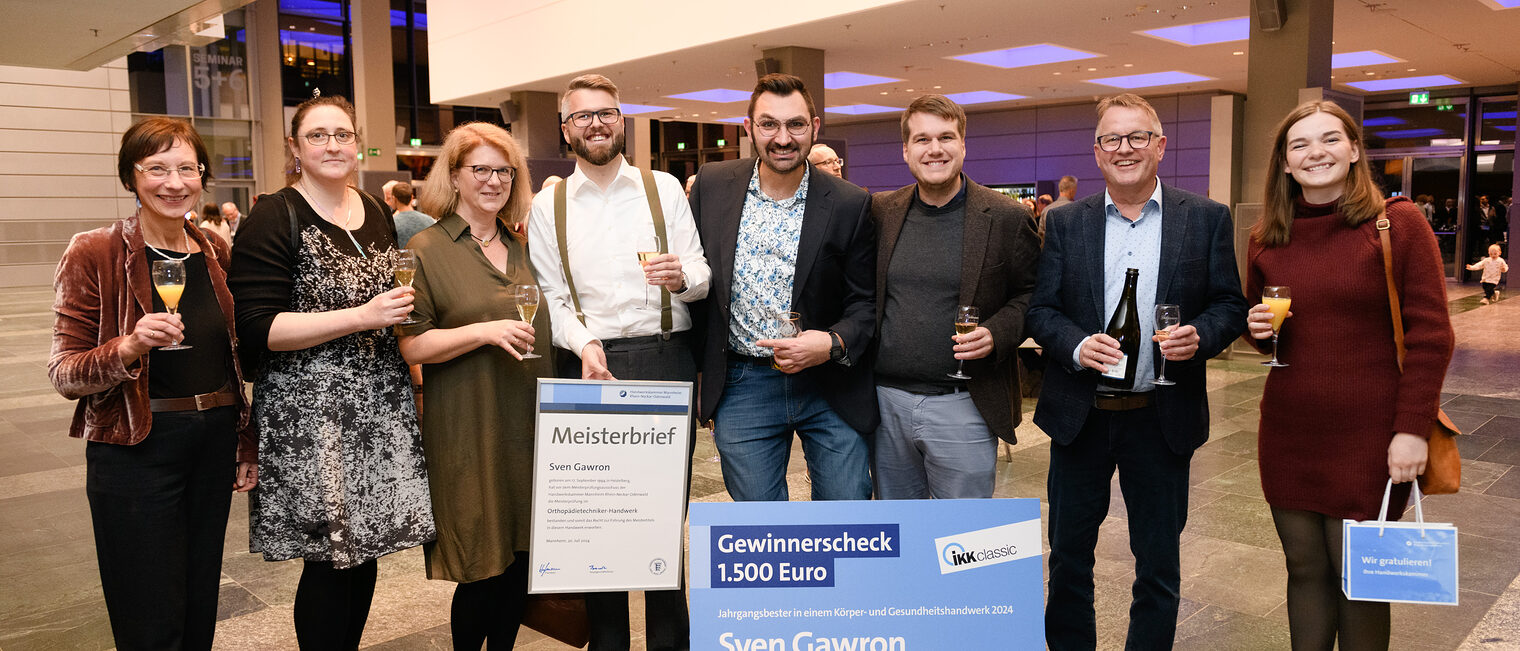 Orthopädietechnikermeister und Preisträger Sven Gawron hält stolz seinen Meisterbrief in der Hand und ist umringt von Freunden und Familie. 