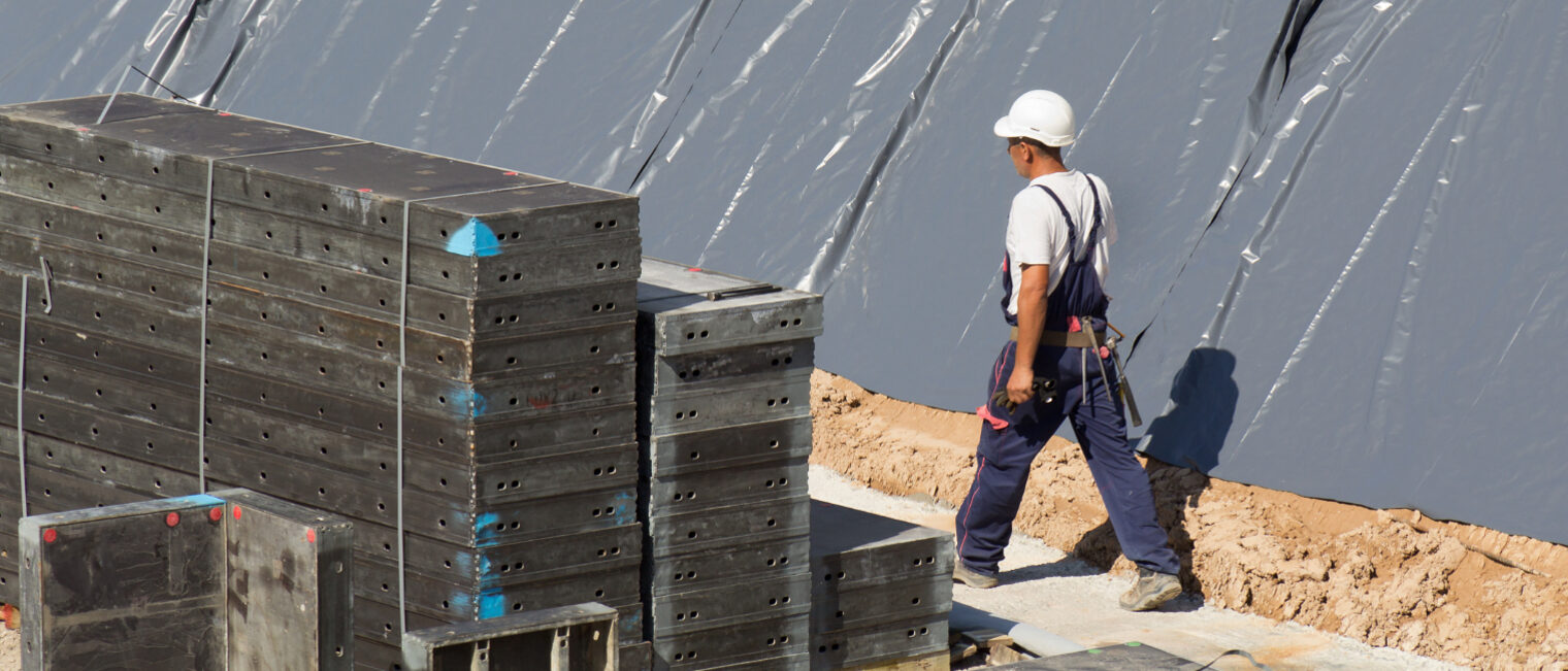 Ein Bauarbeiter mit Helm läuft auf einer Baustelle.
