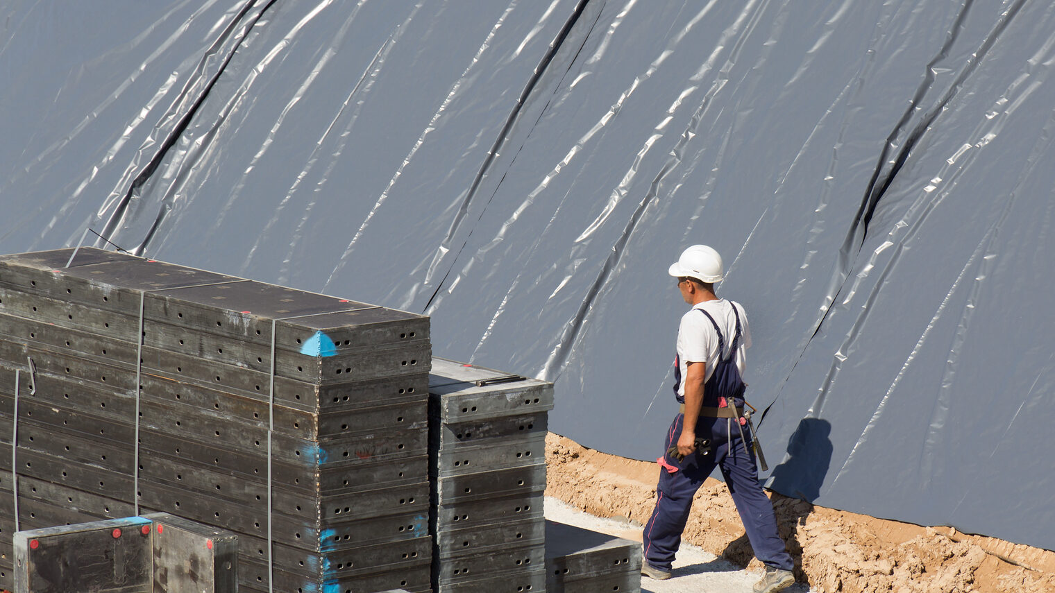 Mann in Latzhose und weißem Helm auf einer Baustelle