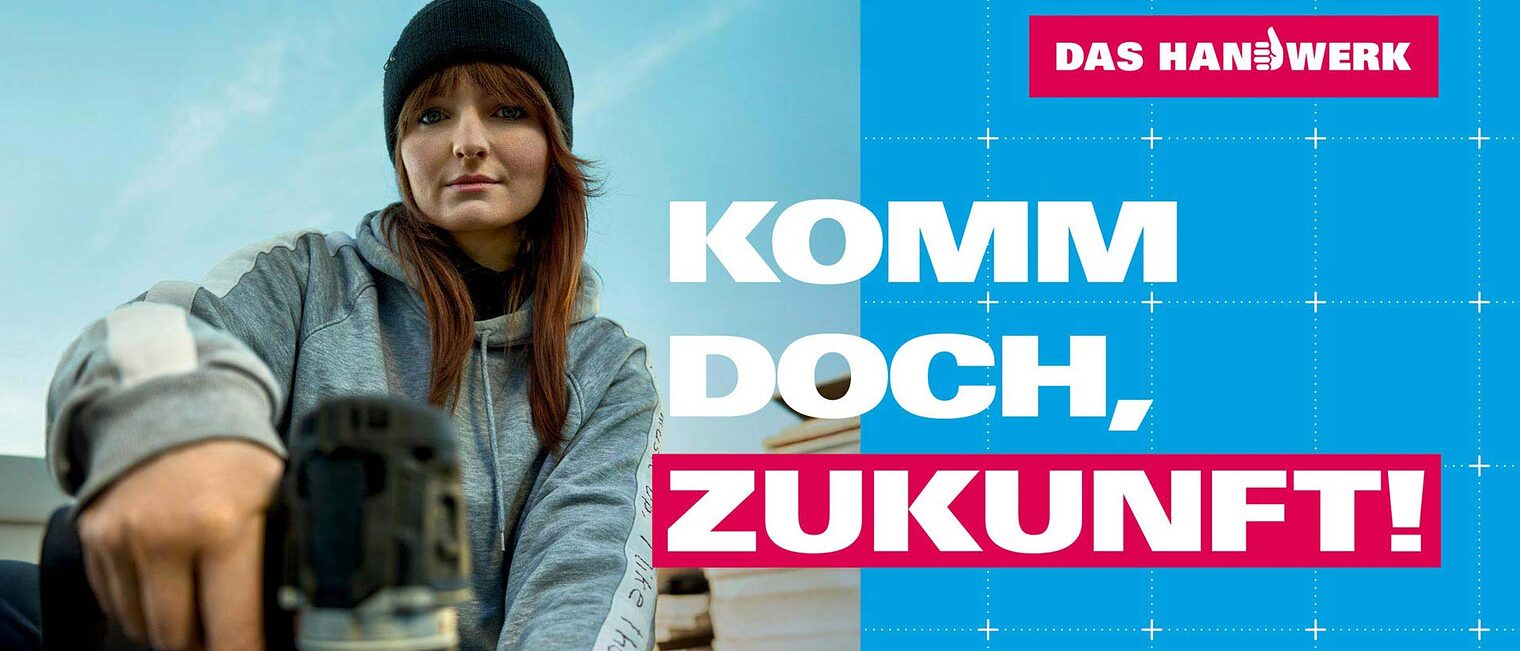 Eine junge Handwerkerin mit dunkler Mütze arbeitet mit einem Akuschrauber und blickt dabei zufrieden lächelnd in die Kamera.