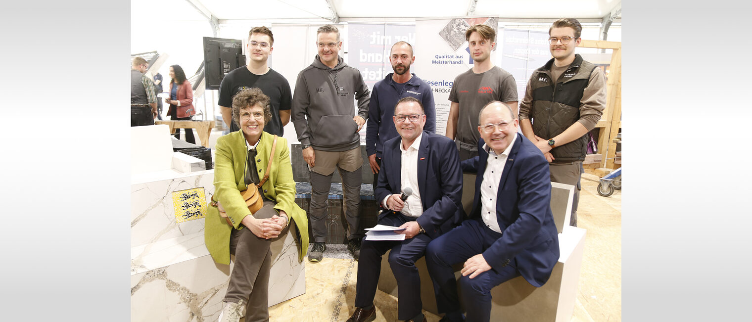 Eröffnung Maimarkt 2025 Frau Felder, OB Specht und Klaus Hofmann sitzend auf den gespendeten Bänken stellten sich zusammen mit Fliesen- und Mosaiklegern (stehend im Hintergrund) dem Fotografen.