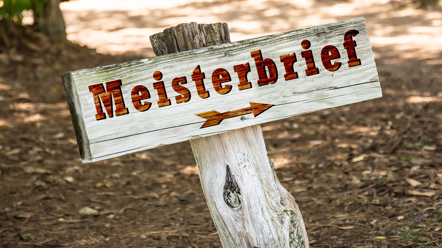 Holzschild mit der Aufschrift "Meisterbrief" und einem Pfeil, das wie ein Wegweiser draußen in der Natur steht