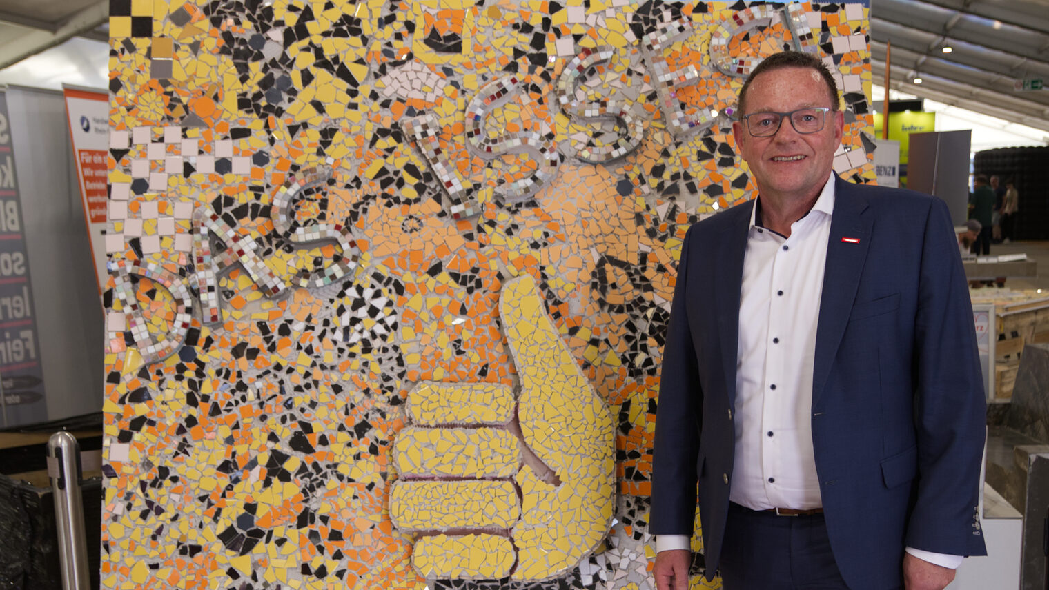 Präsident der Handwerkskammer Mannheim Klaus Hofmann vor buntem Mosaik mit Daumen-hoch-Motiv und dem Schriftzug Das Handwerk