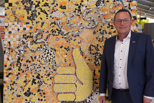 Präsident der Handwerkskammer Mannheim Klaus Hofmann vor buntem Mosaik mit Daumen-hoch-Motiv und dem Schriftzug Das Handwerk