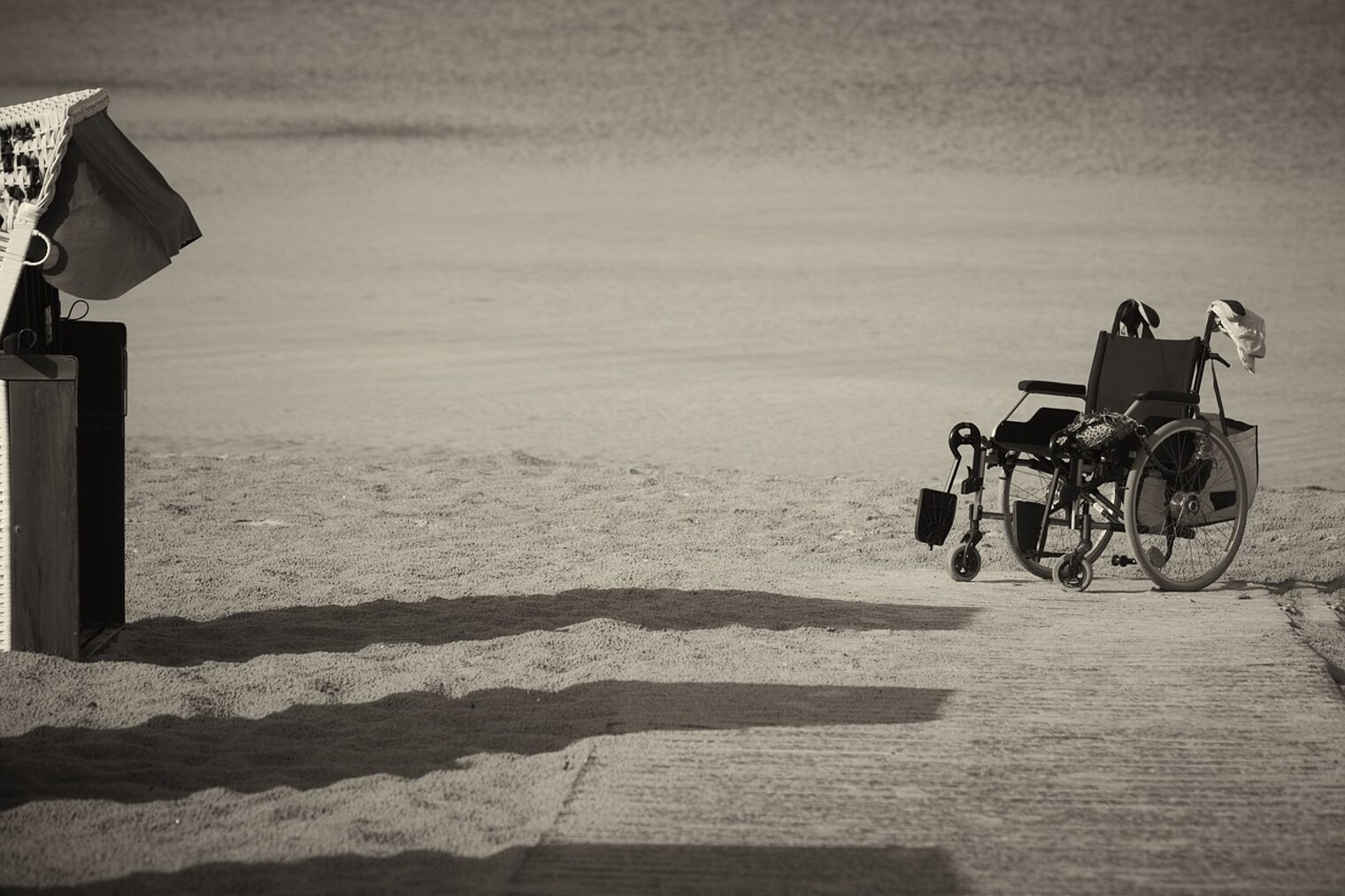 verlassener wheelchair-Rollstuhl an einem Sandstrand neben einem Steg