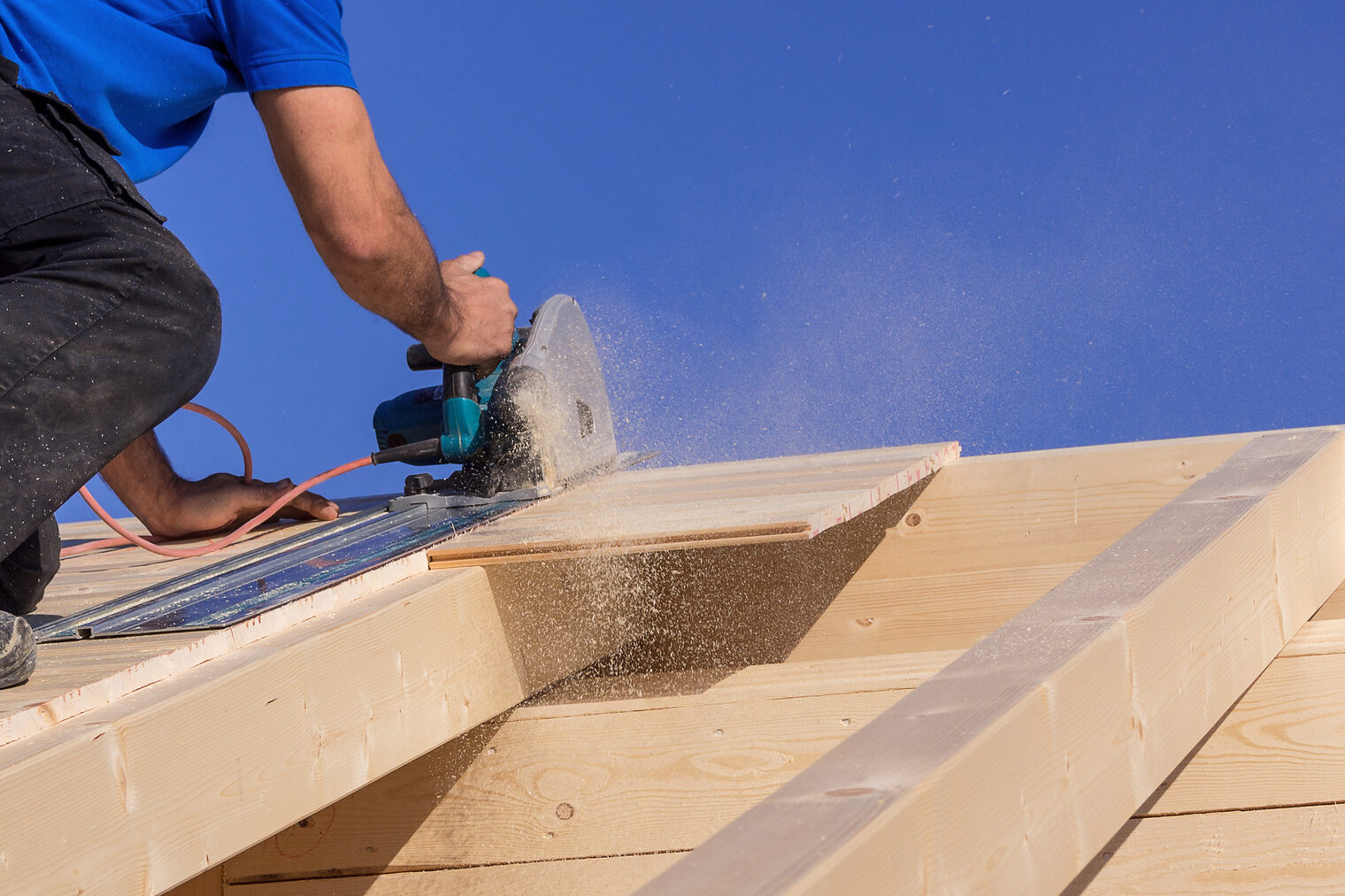 Handwerker sägt auf einem Dach mit Kreissäge bei Sonnenschein, Holzspäne fliegen