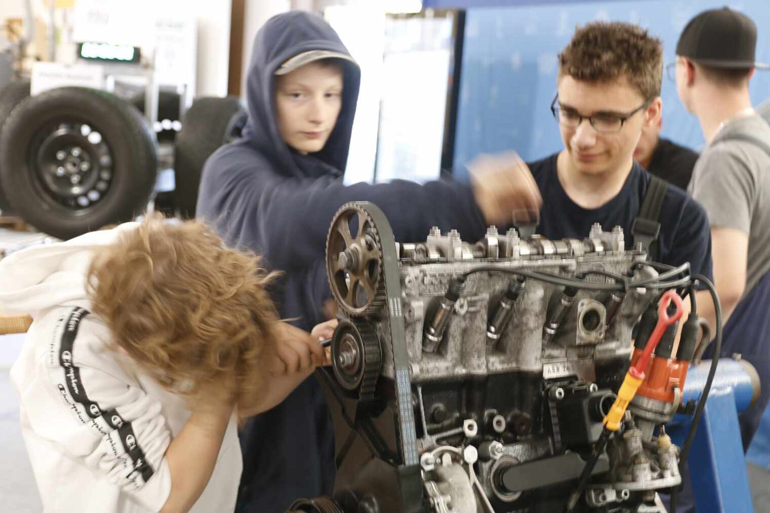 Schüler stehen rund um einen Motor, der linke Junge ist ganz vertieft beim Schrauben, wärend die anderen beiden lächelnd zuschauen