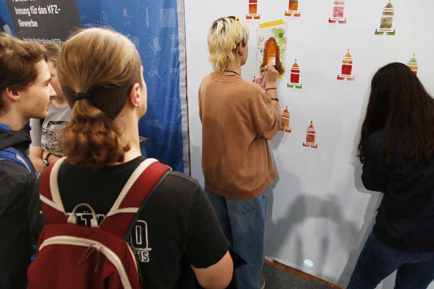 Schülerin betuft durch eine Schablone mit dem Pinsel eine weiße Wand mit Turmmotiven, im Vordergrund weiter Schüler, die sie beobachten