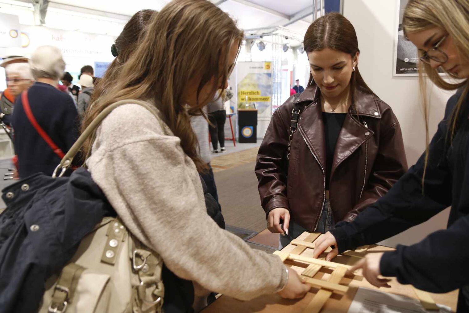Drei junge Frauen stehen im Halbkreis an der Ecke eines Tisches und legen mit konzentiertem Gesichtsausdruck Holzstücke übereinander