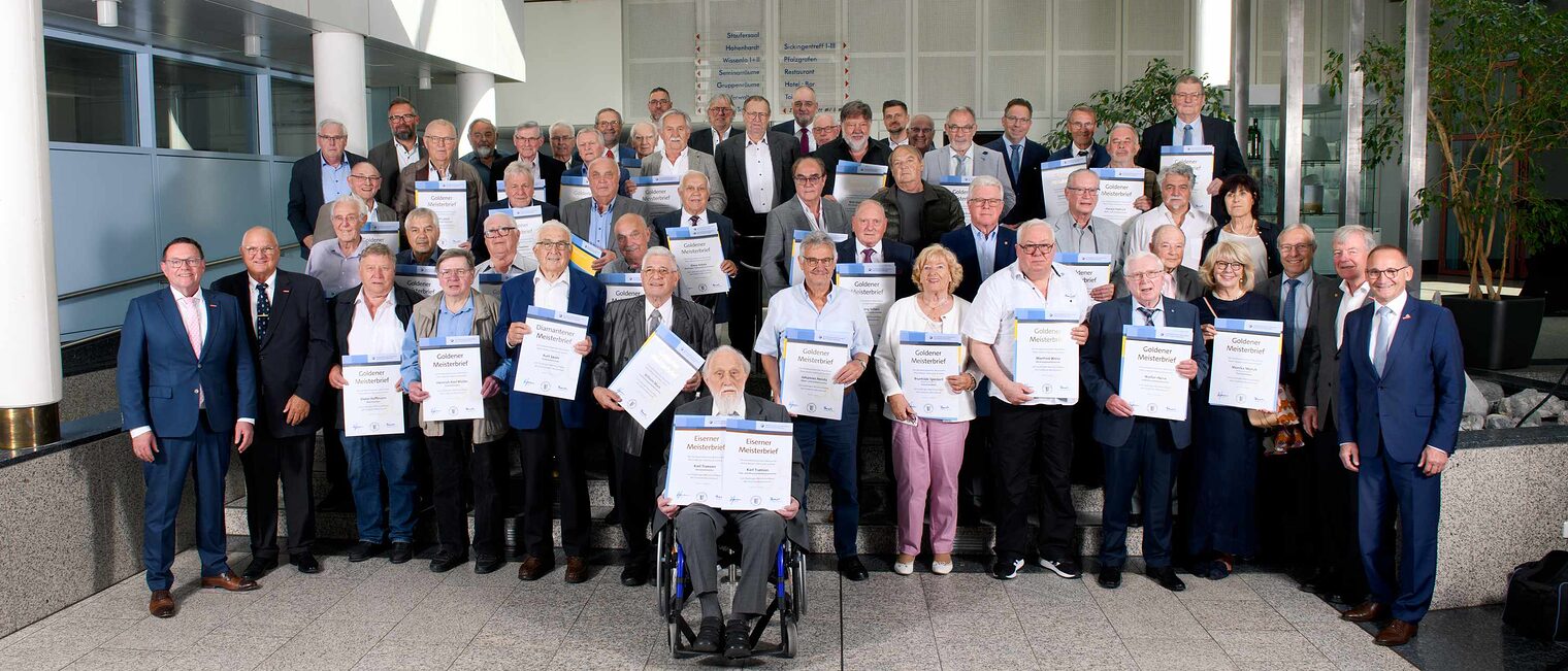 Auszeichnung der goldenen, diamantenen und eisernen Meister durch Handwerkskammer Mannheim Große Gruppe von Senioren in einer Festsaal-Aula, jeweils mit Ehrenurkunden in den Händen, ganz vorne in der Mitte ein Herr im Rollstuhl