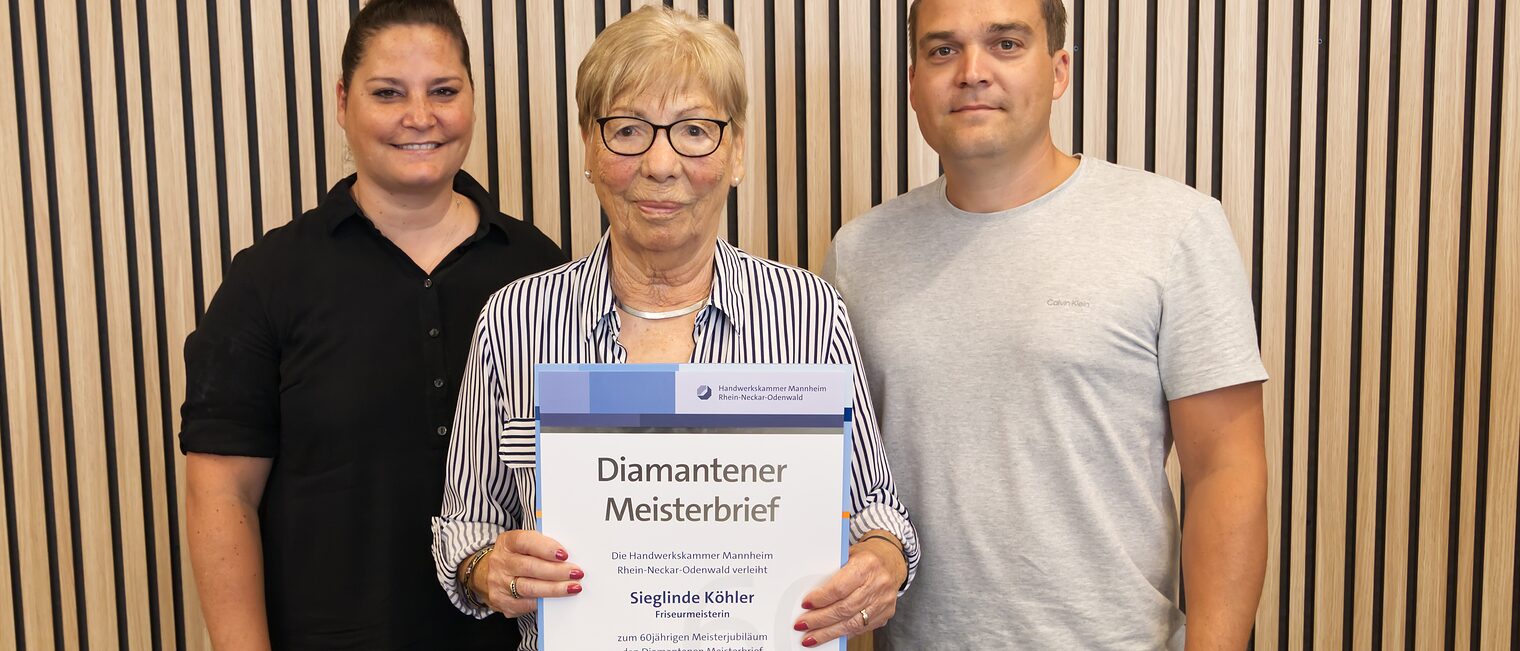Eine Jubilarin steht in der Mitte zwischen zwei Jüngeren Begleitpersonen und hält ihre Urkunde