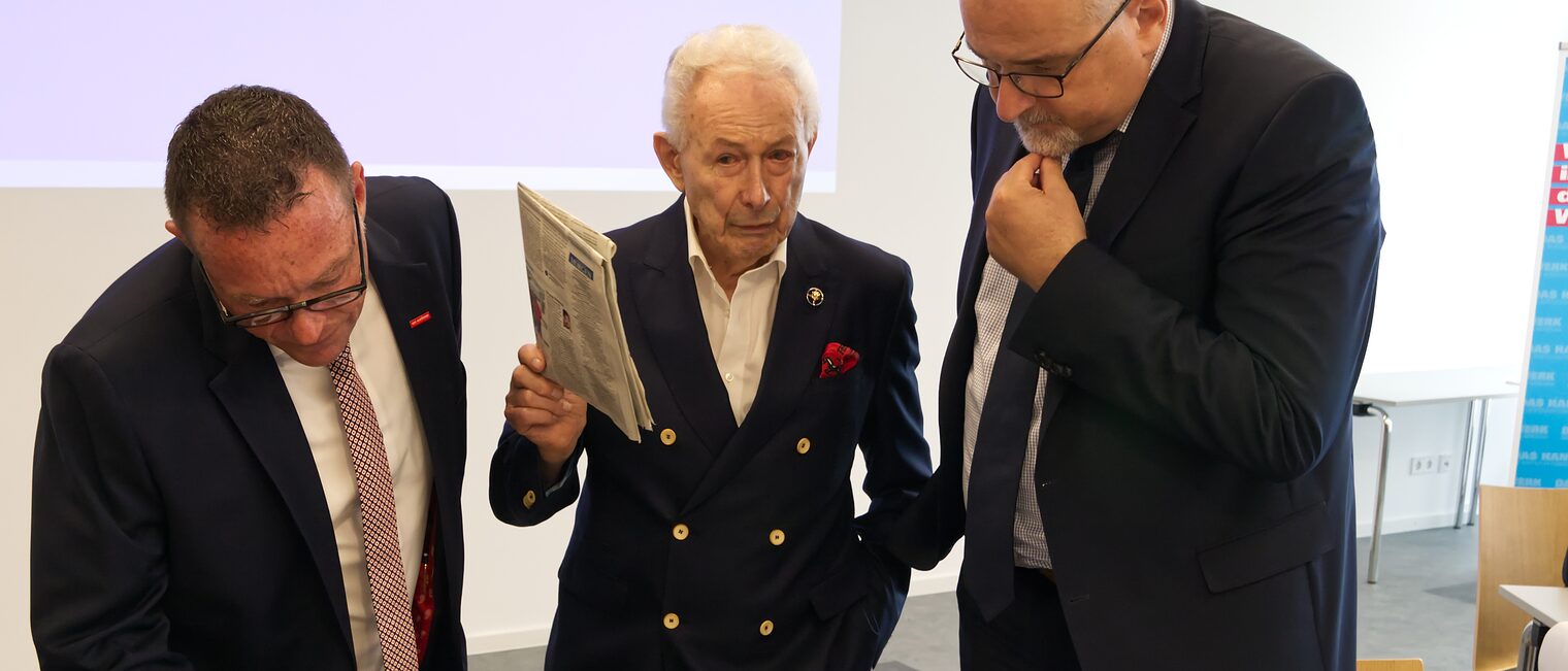 Ein Jubilar steht zwischen Präsident Klaus Hofmann und Hauptgeschäftsführer Jens Brandt, es wird eine alte Urkunde bestaunt