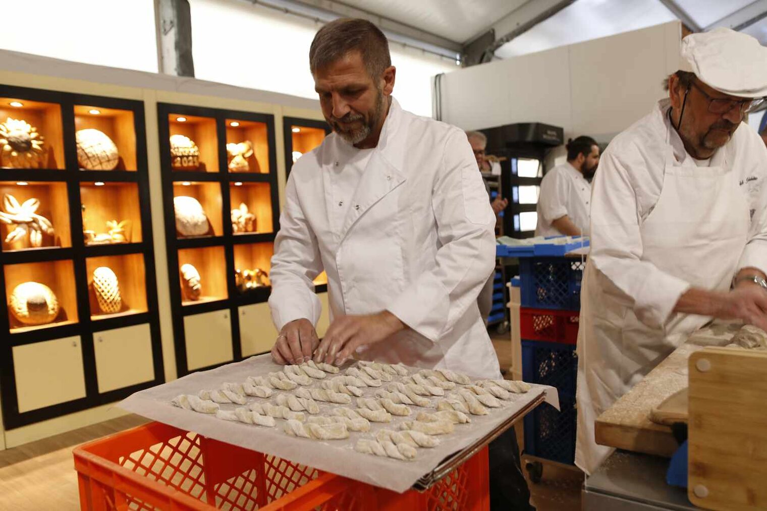 Zwei Bäcker beim Formen von Teig zu kleinen Teigwaren, die auf einem Blech drapiert liegen und zum Ausbacken vorbereitet werden