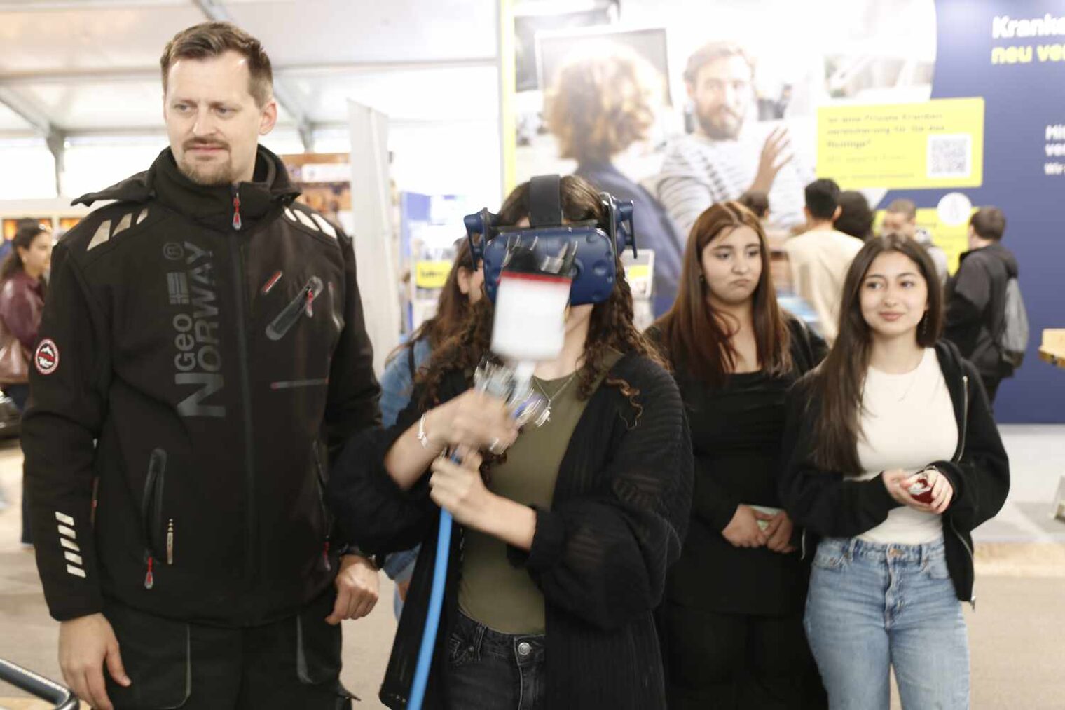 Mädchen führt auf der Messe eine Spritzpistole vor sich her; links neben ihr ein größerer Mann, recht hinter ihr zwei Mädchen