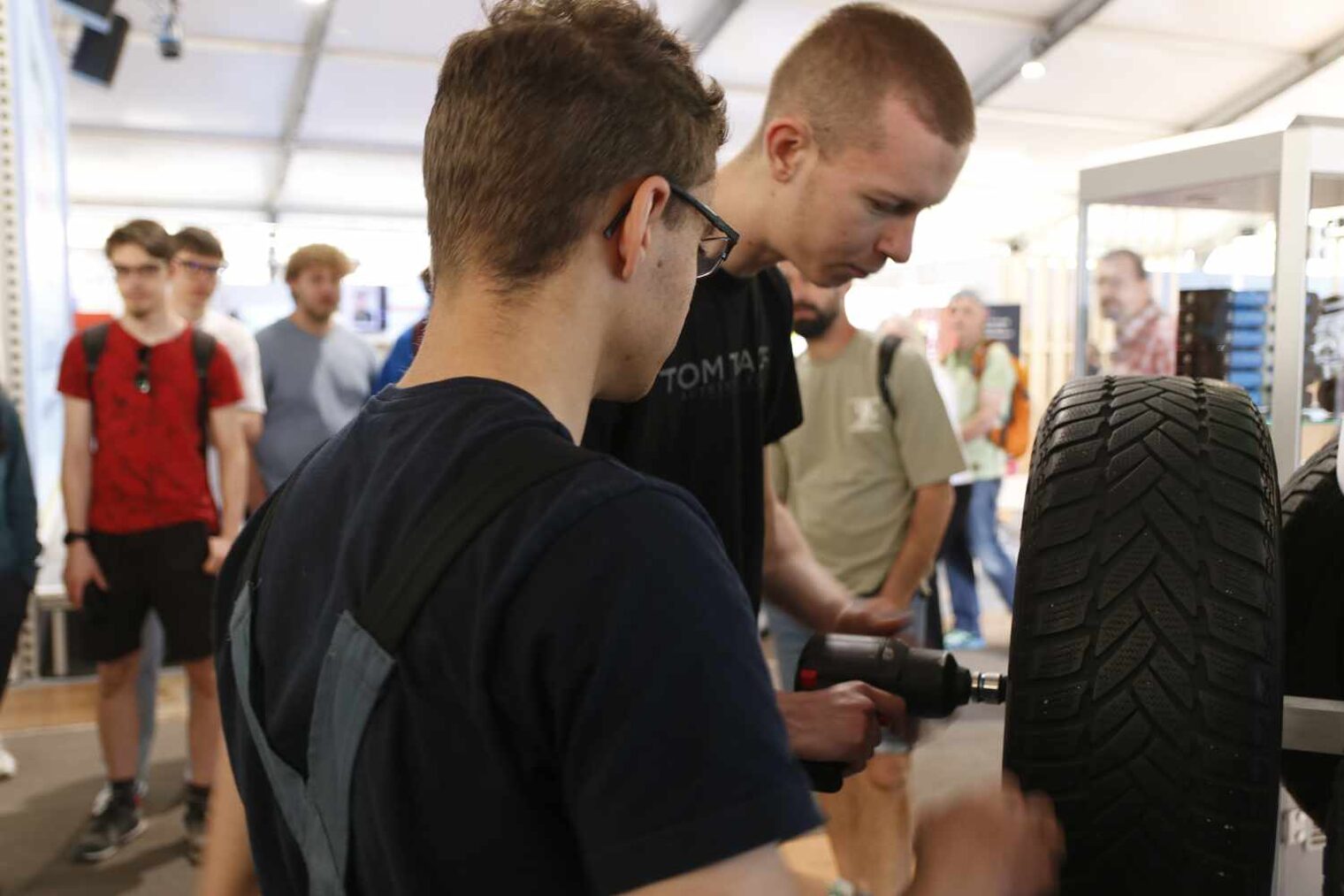 Zwei Männer schrauben mit einem Akuschrauber ein Rad an einer Halterung an, im Hintergrund Messebesucher, die sie beobachten