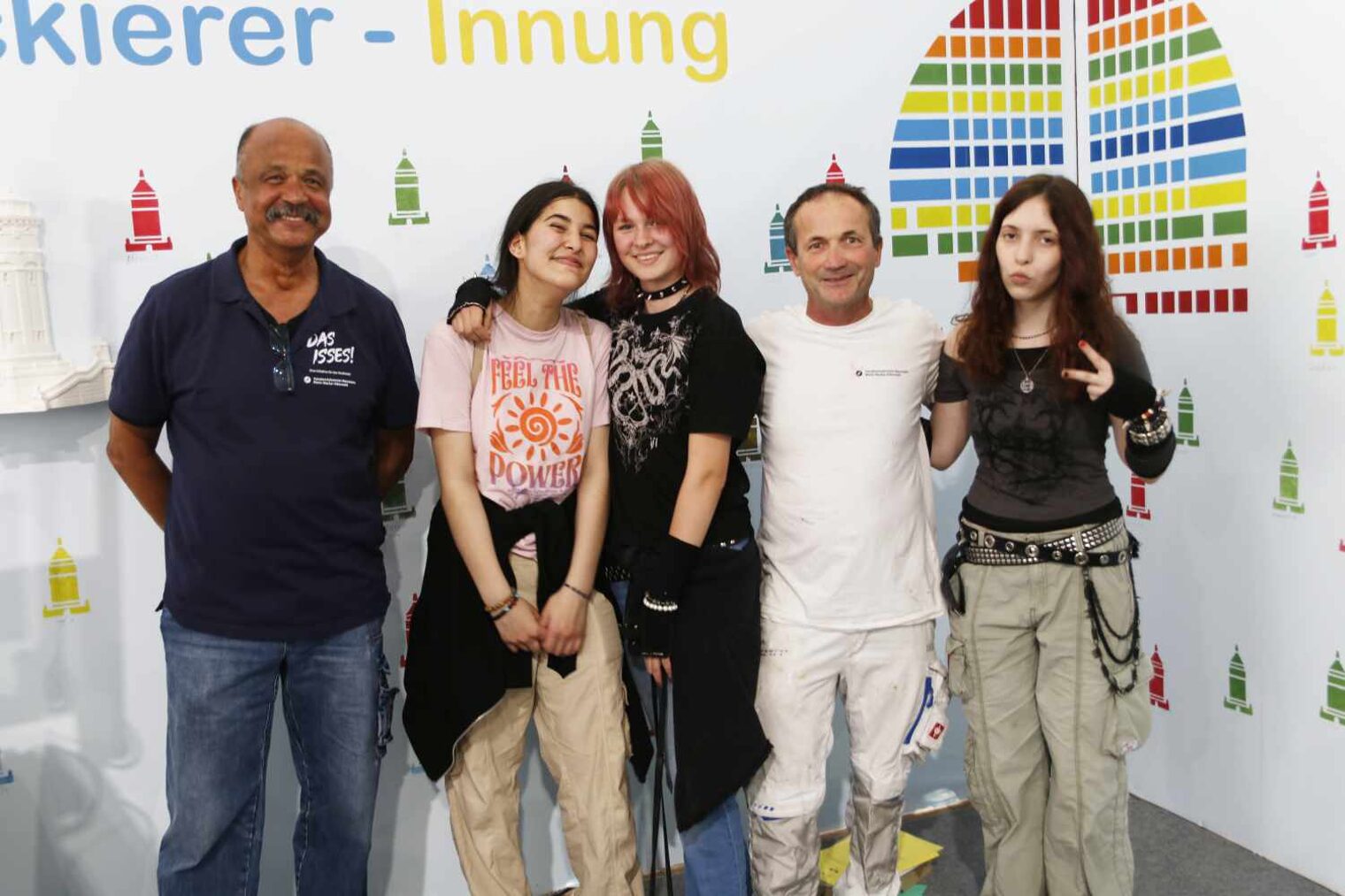 Gruppe von Personen, die in die Kamera lachen - links ein dunkelhäutiger Mann, dann zwei Mädchen, ein Maler und noch ein Mädchen