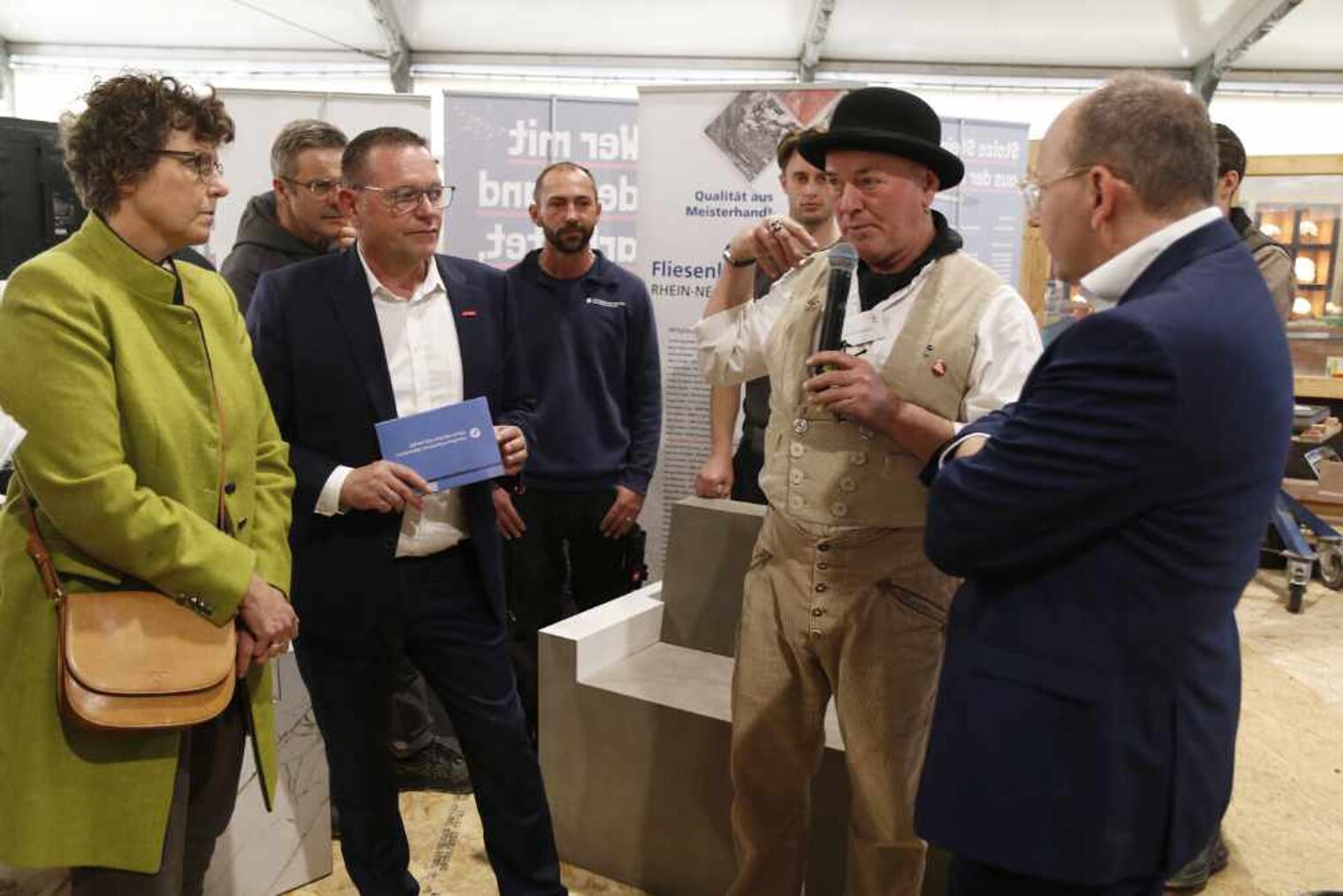 Personen stehen im Halbrund, links Frau im grünen Mantel, daneben Mann mit Moderationskarte in der Hand, daneben ein Steinmetz, dann noch ein Mann