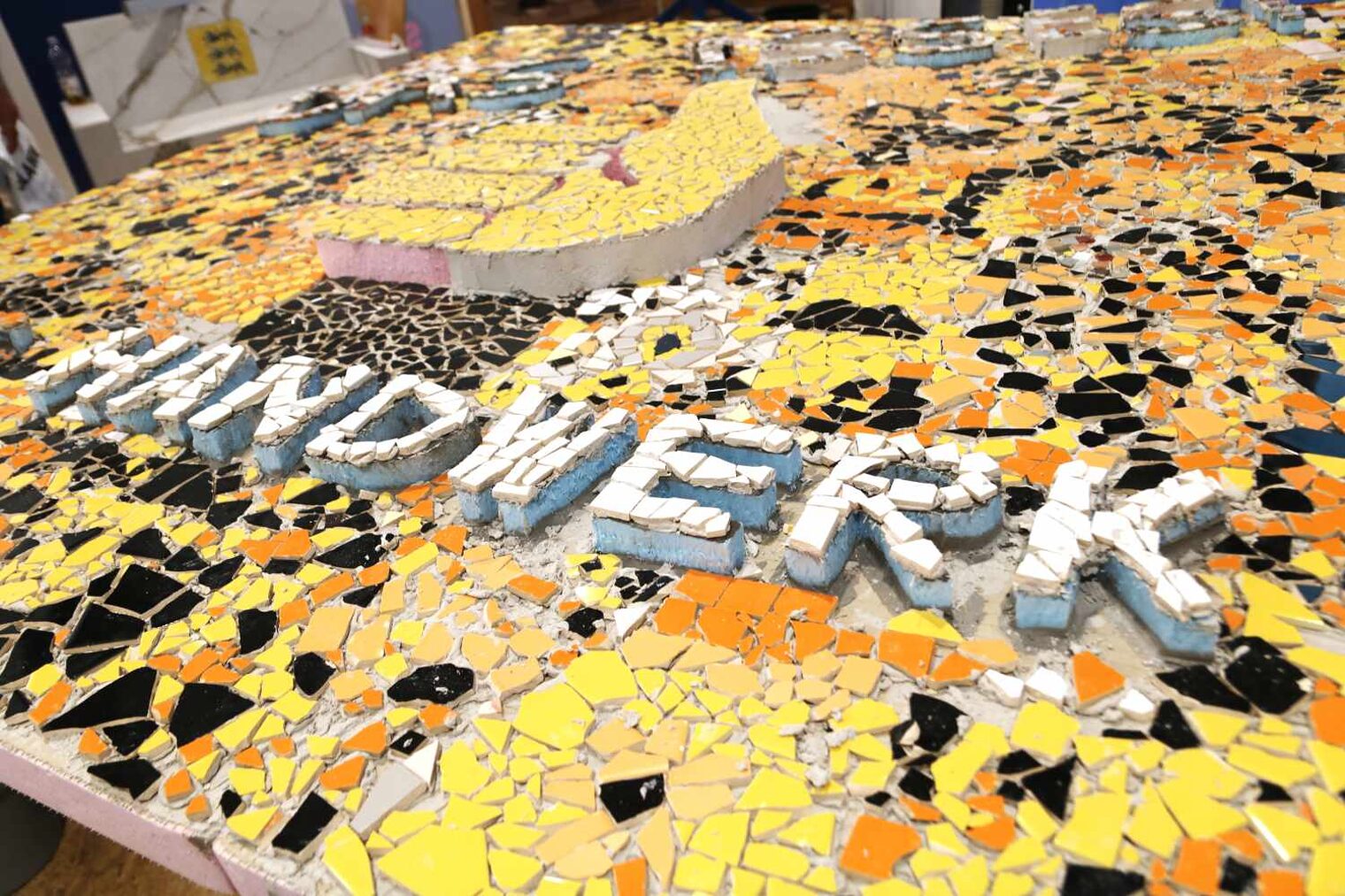 Buntes Bild aus Fliesenbruchstücken in gelben, weißen, orangenen und schwarzen Farben, Schriftzug Handwerk und ein Daumen-Symbol