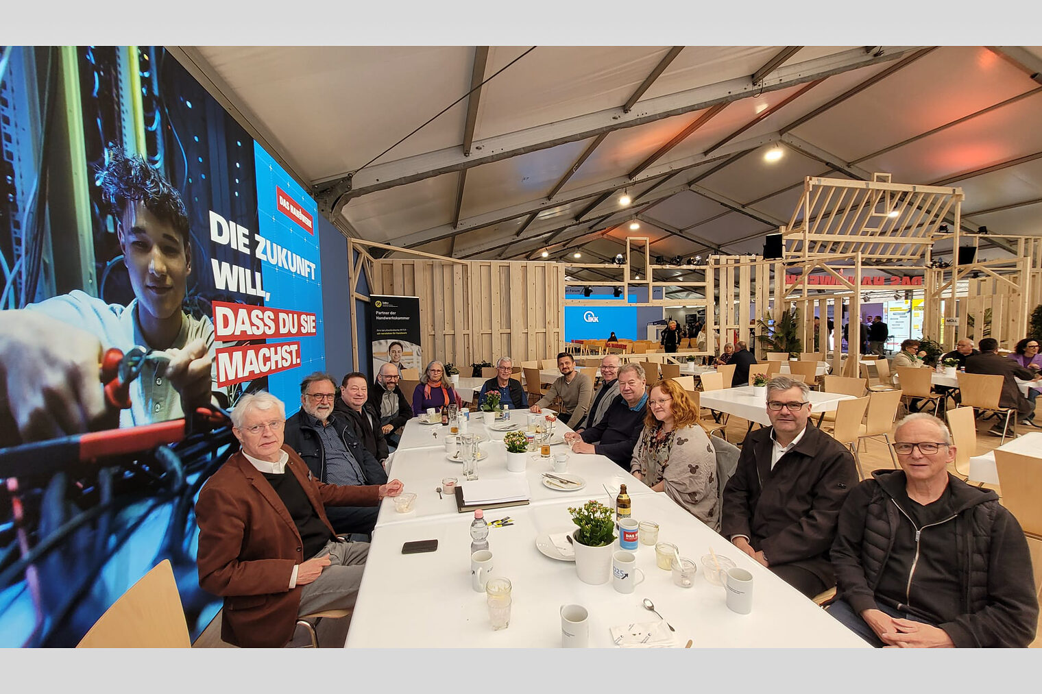 Zehn Vorsitzende sitzen zusammen mit dem Leiter der Meisterprüfungsabteilung an einem langen Tisch und schauen in die Kamera. 