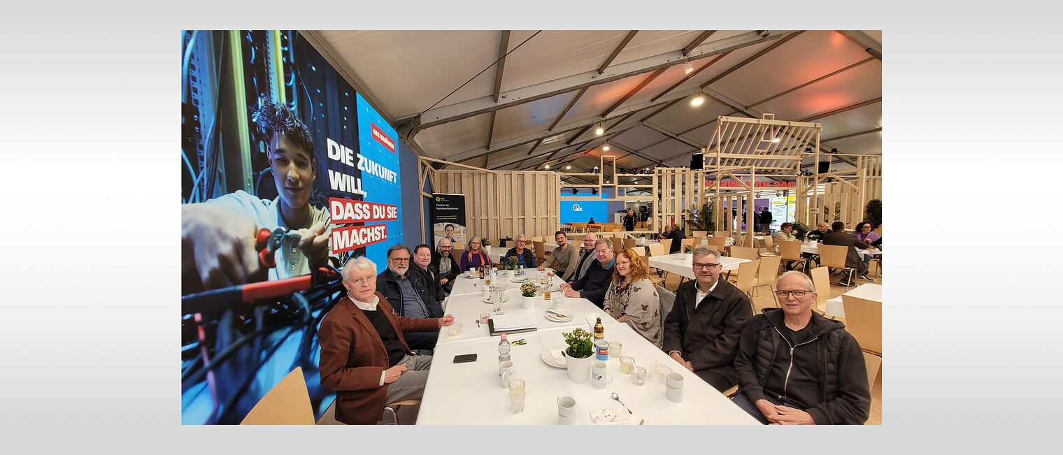 Traditionelles Treffen der Vorsitzenden der Meisterprüfungsausschüssen Zehn Vorsitzende sitzen zusammen mit dem Leiter der Meisterprüfungsabteilung an einem langen Tisch und schauen in die Kamera.