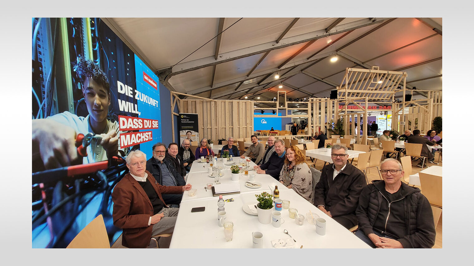 Zehn Vorsitzende sitzen zusammen mit dem Leiter der Meisterprüfungsabteilung an einem langen Tisch und schauen in die Kamera. 